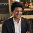 Karthikeya Veeramallu smiling, in a black suit and white shirt